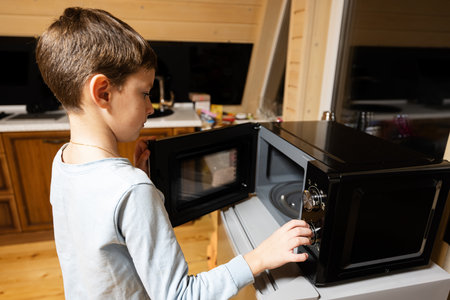 Boy uses the microwave oven in the kitchen.の写真素材
