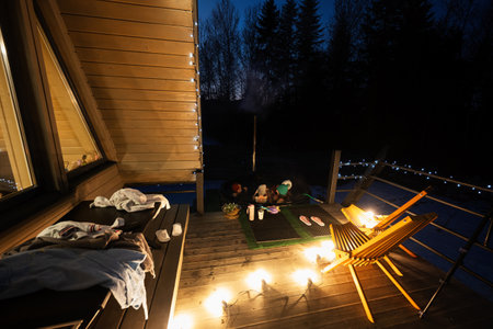 Family enjoying bathing in wooden barrel hot tub in the terrace of the cottage. Scandinavian bathtub with a fireplace to burn wood and heat water.の写真素材