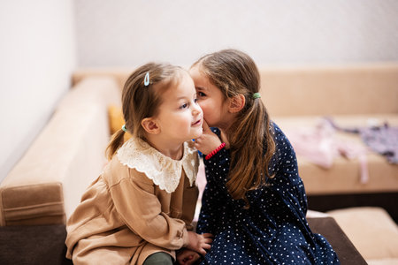 Two sisters sit on the sofa and tell and share girlish secrets with each other.の写真素材