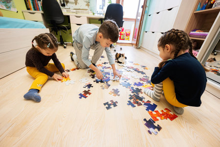 Children connecting jigsaw puzzle pieces in a kids room on floor at home.  Fun family activity leisure.の写真素材