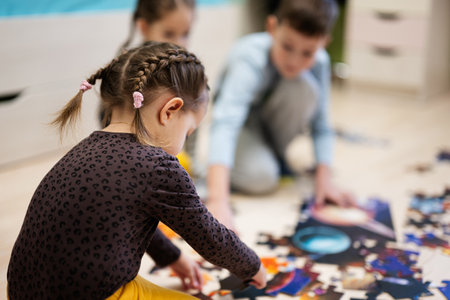 Children connecting jigsaw puzzle pieces in a kids room on floor at home.  Fun family activity leisure.の写真素材
