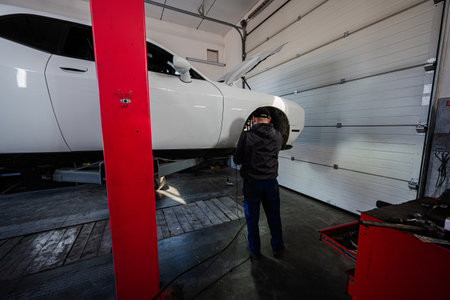 Mechanic in service repair station working with muscle car, dismantles a wheel on lift.の写真素材