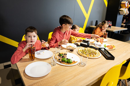 Four kids eating italian pizza in pizzeria. Children eat at cafe. Boy drink juice.の写真素材