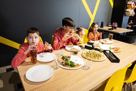 Four kids eating italian pizza in pizzeria. Children eat at cafe. Boy drink juice.の写真素材
