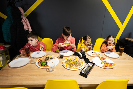 Four kids eating italian pizza in pizzeria. Children eat at cafe.の写真素材
