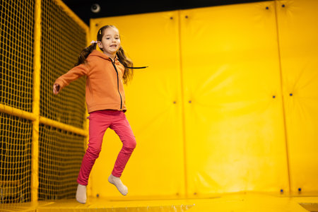 Little girl kid jumping on trampoline at yellow playground park. Child in motion during active entertaiments.の写真素材