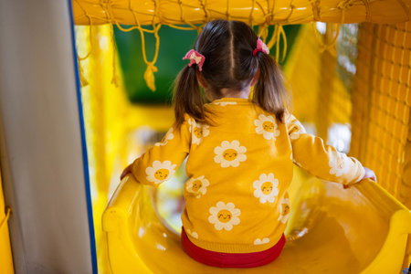 Back of baby girl kid slide at yellow playground park. Child in active entertaiments.の写真素材