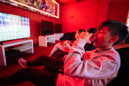 Two boys gamers play football gamepad video game console in red gaming room. Drink soda can.の写真素材