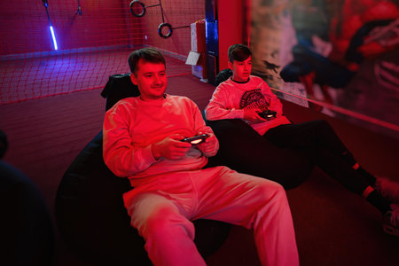 Father and son play gamepad video game console in red gaming room. Dad and kid gamers.