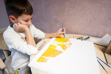 Left handed boy is painting by numbers with gouache at home.の写真素材