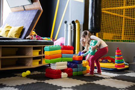 Two sisters playing at kids play center while build with colored plastic blocks.の写真素材
