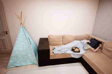 Young woman lying in bed at home and read book with her cat.
