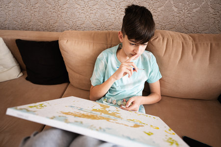 Young male teenager painting picture by numbers on canvas in living room at home. Hobby and leisure...