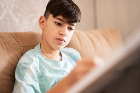 Young male teenager painting picture by numbers on canvas in living room at home. Hobby and leisure concept.の写真素材