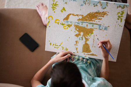 Young male teenager painting picture by numbers on canvas in living room at home. Hobby and leisure concept.の写真素材