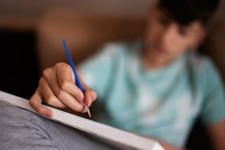 Young male teenager painting picture by numbers on canvas in living room at home. Hobby and leisure...