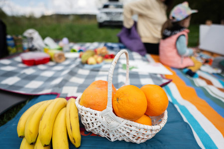 Fruits against happy young family having fun and enjoying outdoor on picnic blanket at garden spring park, relaxation.の写真素材