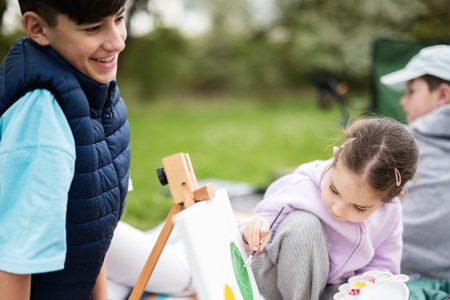 Happy young family, Ñhildren having fun and enjoying outdoor on picnic blanket painting at garden spring park, relaxation.の写真素材