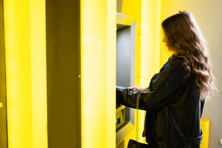 Young brunette girl withdrawing money from credit card at yellow ATM.の写真素材