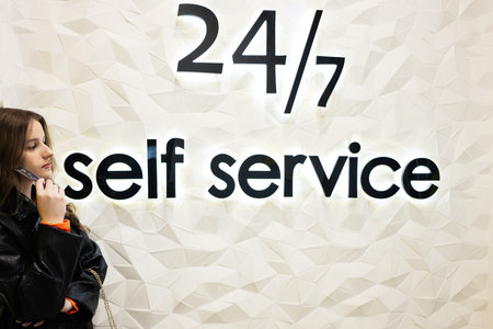 Young brunette girl with credit card against 24 7 self service bank. Round the clock support.の写真素材