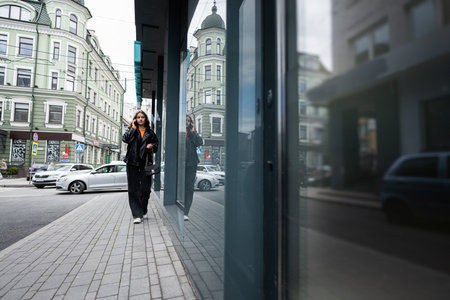 Young lady in leather jacket walking in urban city, speaking on phone.