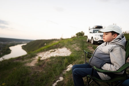 Boy sit on chair, hiking on vacation, having evening picnic on top of the mountain, looking at beautiful canyon landscape.の写真素材