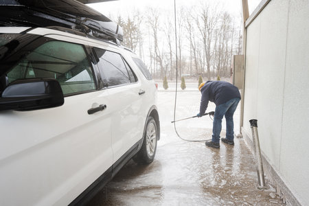 Man washing high pressure water american SUV car with roof rack at self service wash in cold weather.の写真素材