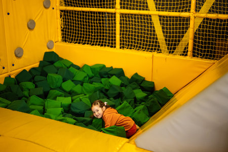 Little girl kid slide to green soft cubes at yellow playground park. Child in active entertaiments.の写真素材