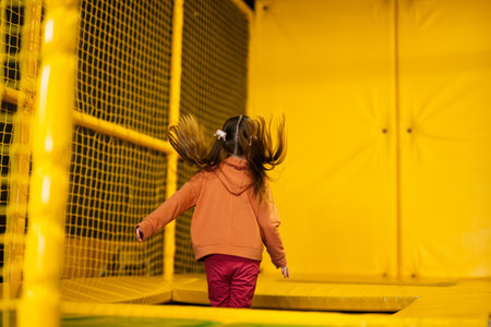 Little girl kid jumping on trampoline at yellow playground park. Child in motion during active entertaiments.の写真素材