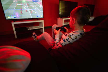 Boy gamer play gamepad football video game console in red gaming room.