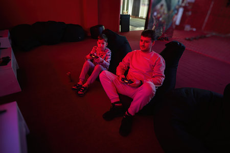 Father and son play gamepad video game console in red gaming room. Dad and kid gamers.