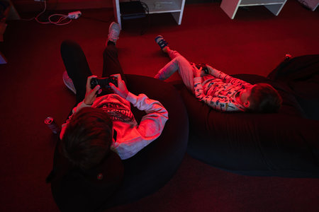 Two boys gamers play gamepad video game console in red gaming room.