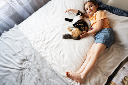 Cute little girl playing with her cat on the bed at homeの写真素材