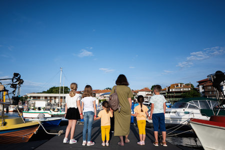Rear view of a group of children with mother standing on the deck of a yacht and looking at the sea.