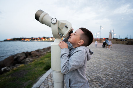 Boy looks at the sea through a coin operated telescope in the evening Nessebar.の写真素材