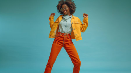 Stylish african american woman in yellow jacket and orange pants on blueの素材