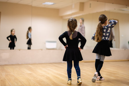 Young girls participate in a dance class, practicing ballet and dance moves in a mirrored studio....