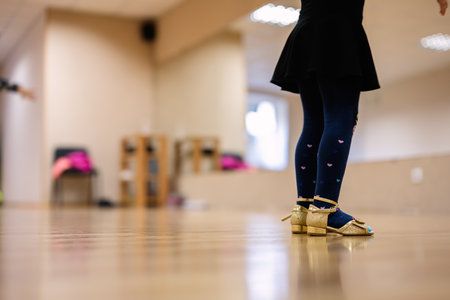 A close-up image showing a young girl wearing golden tap dance shoes in a dance studio setting.の写真素材