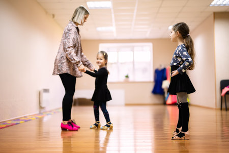 A dance instructor teaches two young girls in a bright and spacious dance studio. The girls wear...