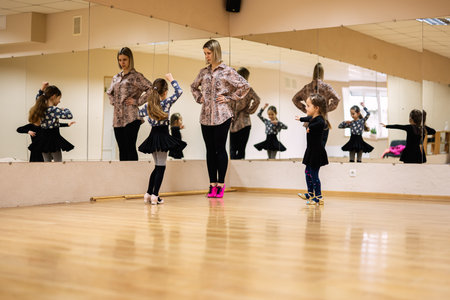 A dance instructor guiding young girls in a ballet studio with mirrored walls, focusing on technique...