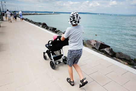Child pushing a stroller along a scenic seaside promenade on a sunny day. A peaceful setting with...
