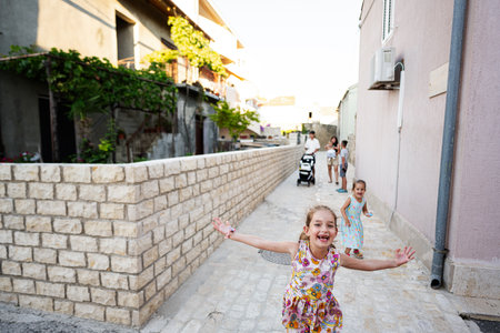 Happy children running and playing in a sunlit alleyway while parents and siblings enjoy the outdoors in Nin, Croatia.の写真素材