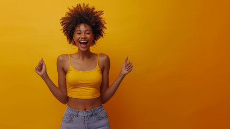 Excited young woman in a yellow top, smiling broadly and pointing fingers up, standing against a vibrant yellow background. Captures joyful and lively emotions.の素材