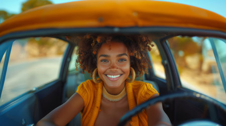 Cheerful young African American woman driving a classic car on a bright sunny day, embodying freedom and happiness.の素材