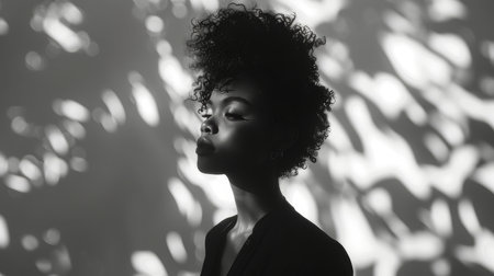 Black and white profile shot of a beautiful African woman with curly hair, showcasing dramatic lighting and artistic shadows.の素材