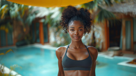 Portrait of young woman in athletic wear, smiling confidently by a tropical pool. Captures fitness, vacation, and lifestyle themes.の素材