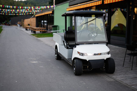 A white golf cart parked on a paved street next to a venue adorned with colorful bunting flags, evoking a festive atmosphere.の写真素材