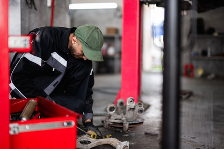 A mechanic in a green cap is focused on repairing a car part in a professional auto workshop, showcasing dedication and technical skill.の写真素材