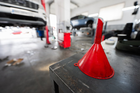 A red funnel placed on a workbench in a busy car repair garage, with vehicles being serviced in the background.の写真素材