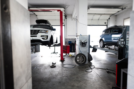 Interior of a modern auto repair shop featuring vehicles on hydraulic lifts. The spacious garage is equipped with tools and machinery for car maintenance and repair.